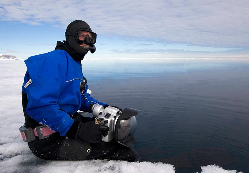 Photographer Paul Nicklen sitting on the edge of an ice floe.